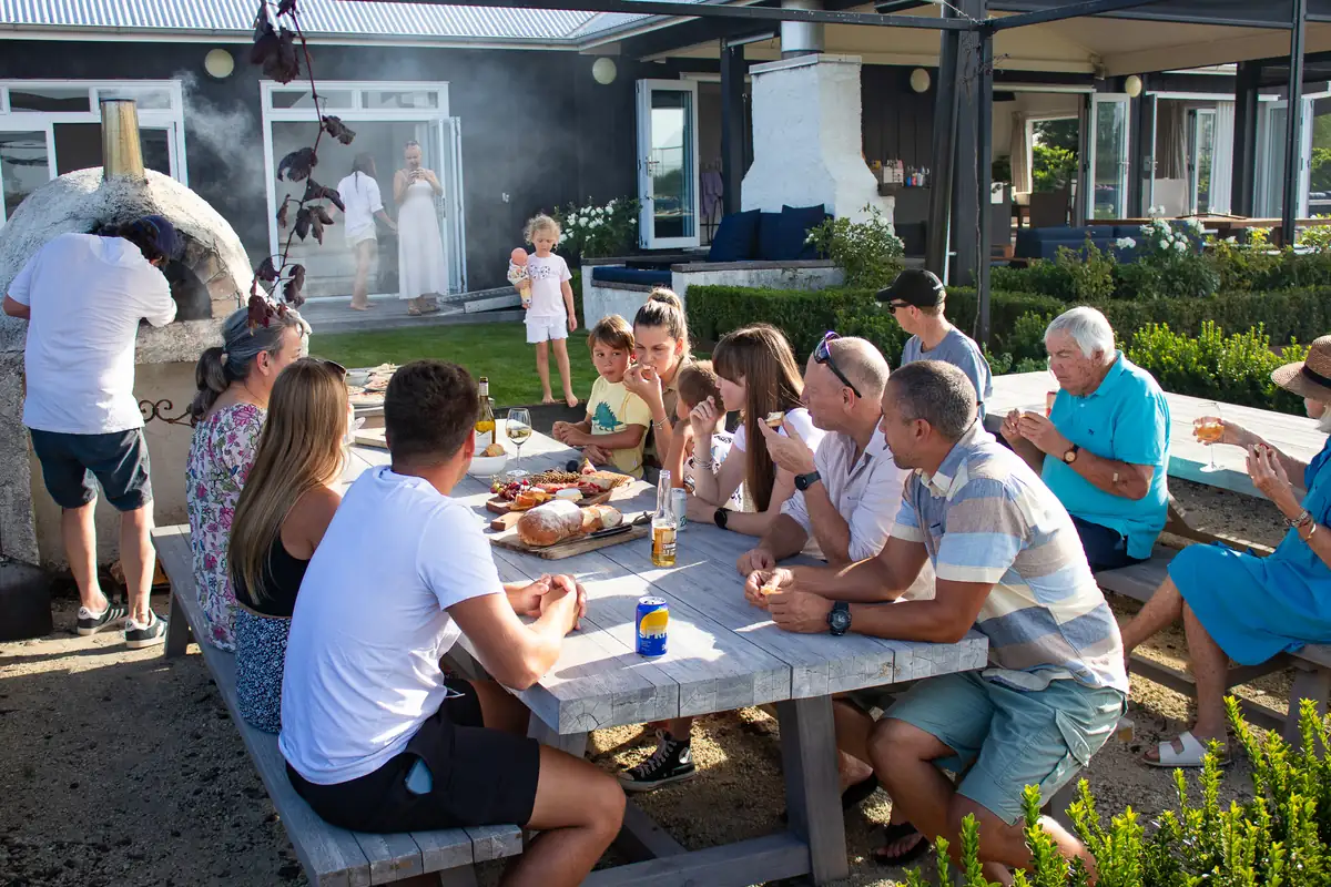 An intergenerational family group gathered around at a table in the pizza oven area of Lawn Road Retreat.