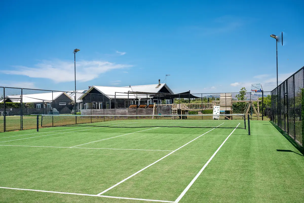 View of the tennis court with the house and playground area in the background at Lawn Road Retreat
